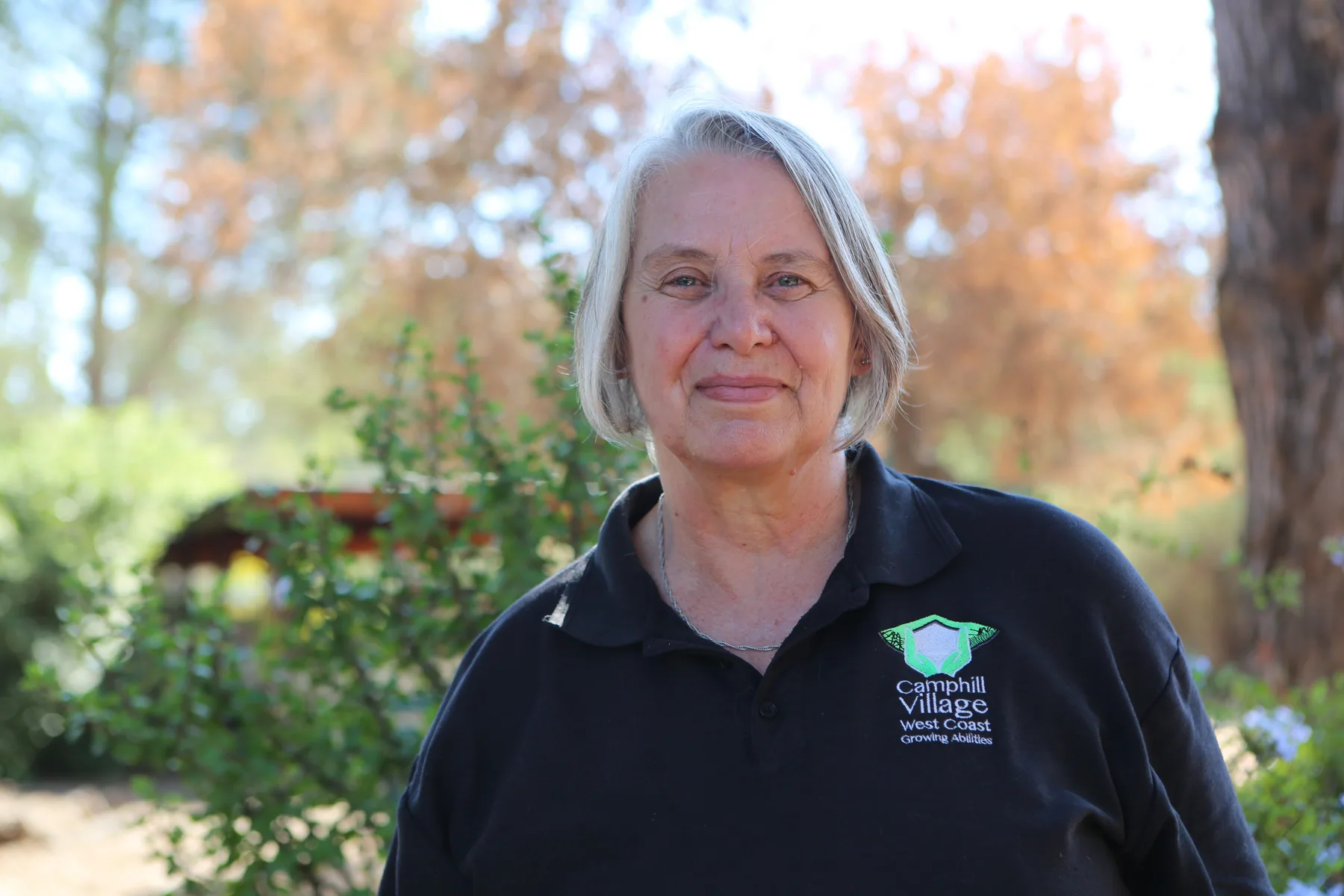 Annett from the Camphill Village social work office, wearing a Camphill Village West Coast shirt, photographed in the village gardens