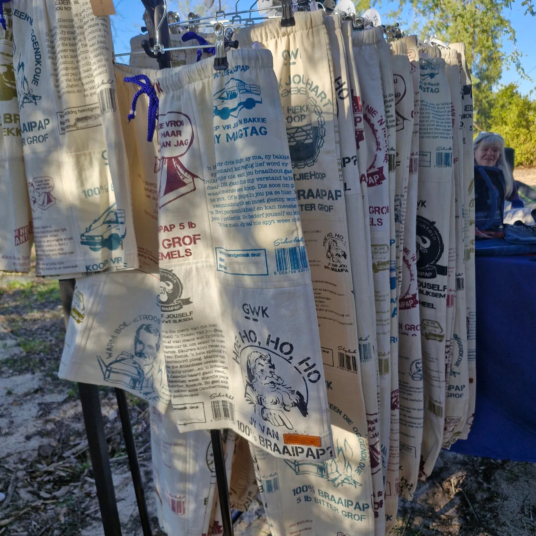 Shorts hand sewn from printed maize meal sacks, hanging in rows on a rail at an outdoor market stall