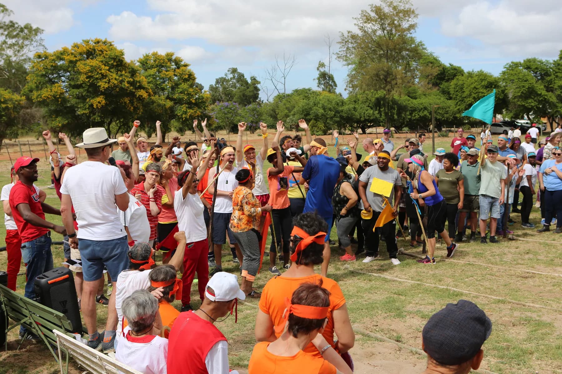 Residents, co-workers and volunteers packed together on the sports field at Camphill Village, cheering with their arms raised as a teal flag flies behind them.