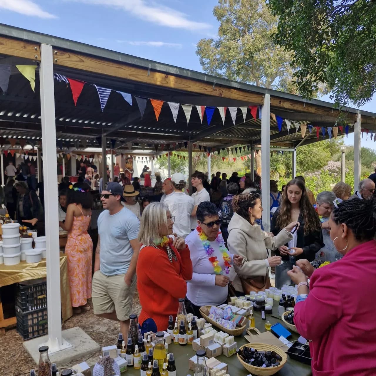 Shoppers browsing stalls under a covered walkway strung with bunting at the Camphill market