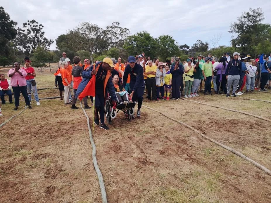 A crowd of residents, families and staff lining the village field on sports day, applauding as a group makes its way along the marked track.