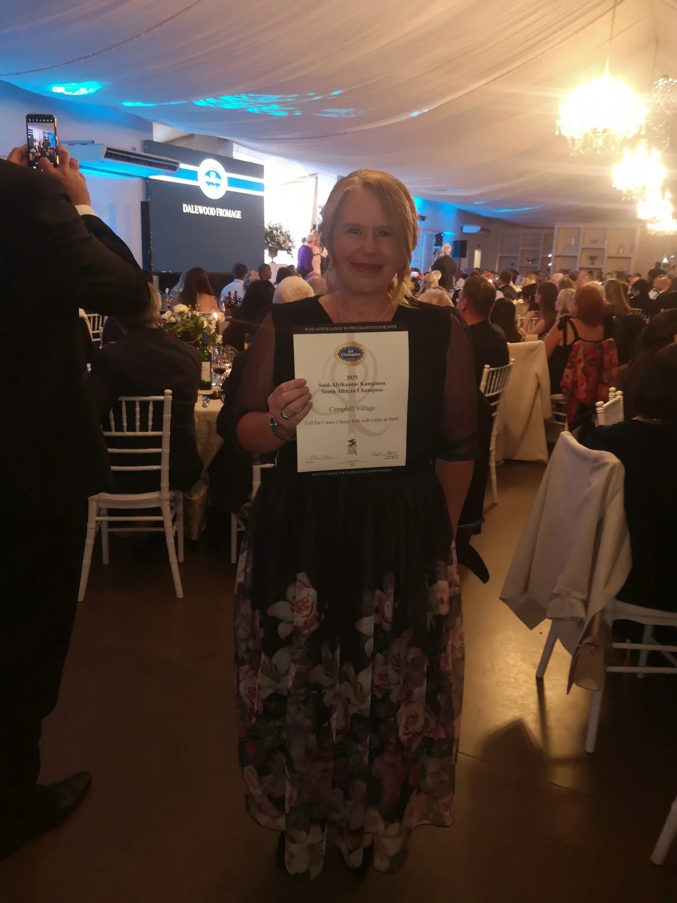 A Camphill staff member holding up a framed award certificate at an evening awards dinner